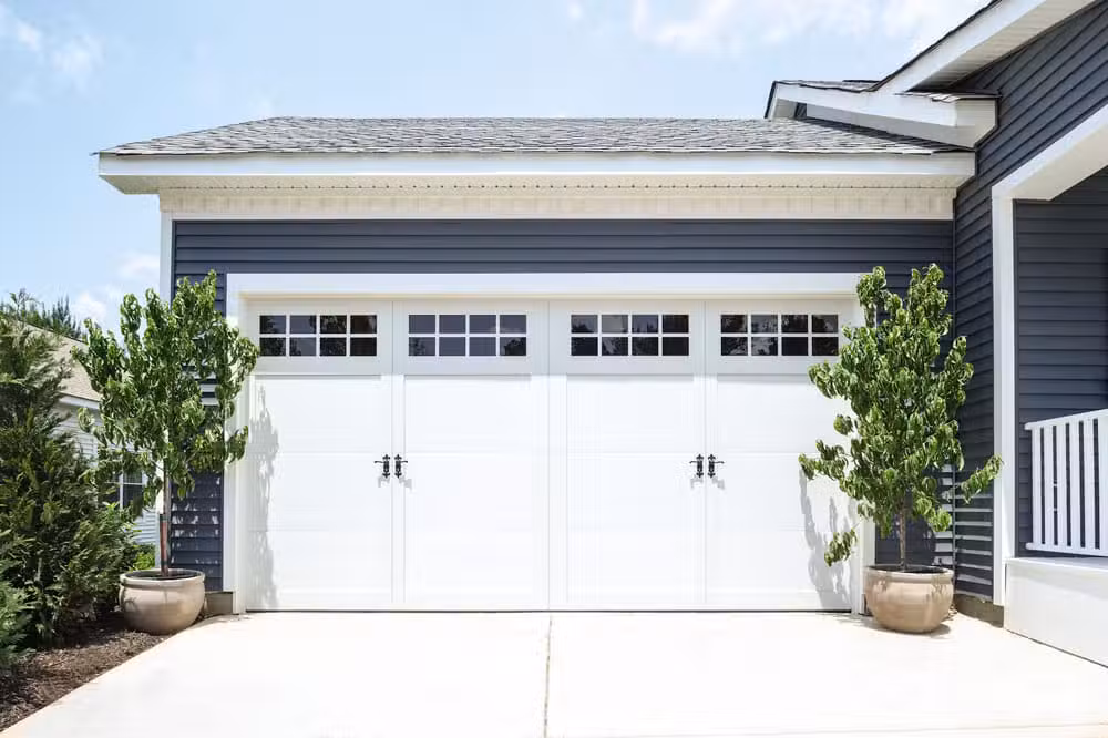 White carriage-style garage doors with windows on a gray house with blue-gray vinyl siding