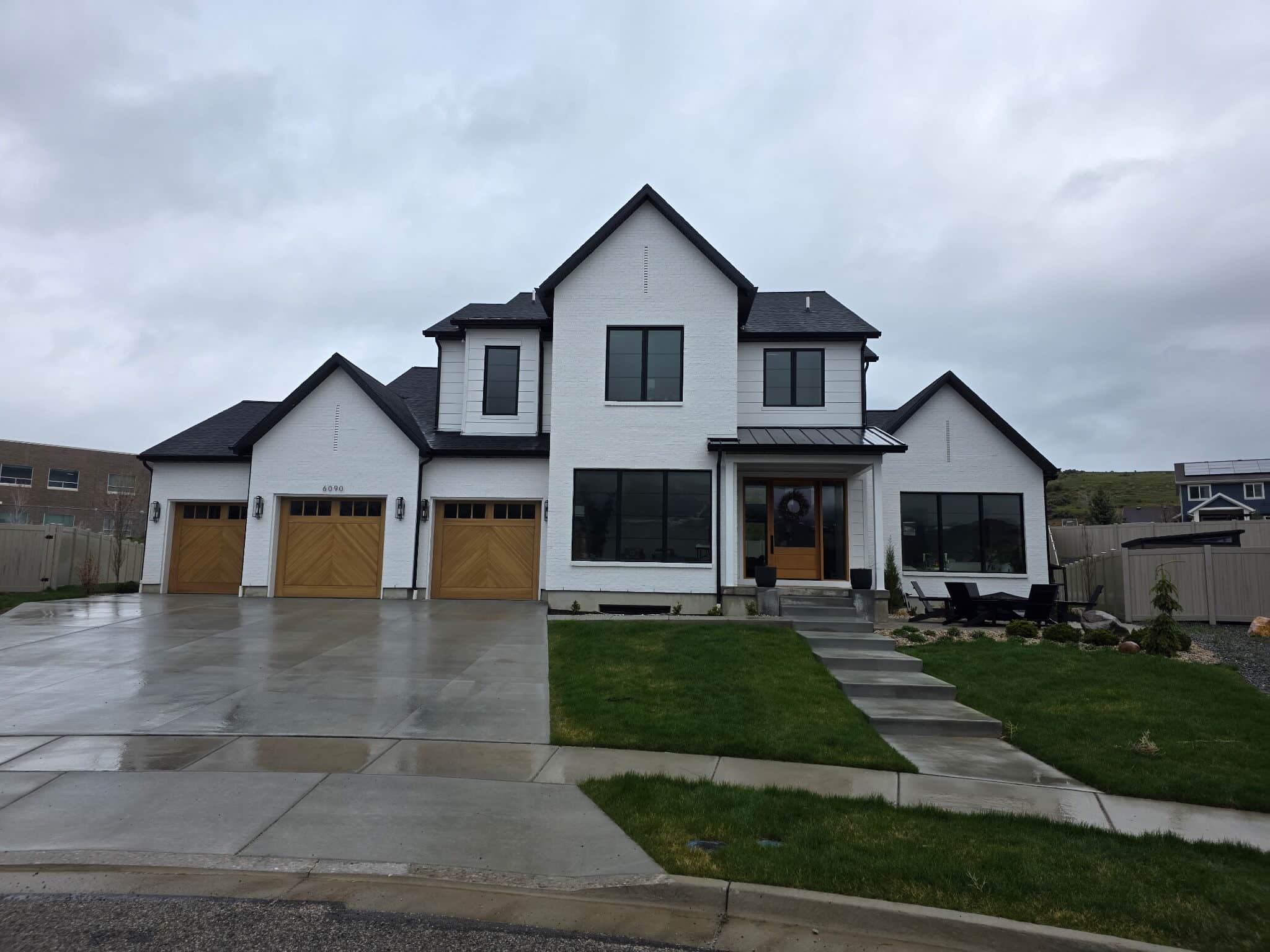 Three wood-finish carriage-style garage doors with chevron panels on a white painted-brick modern farmhouse
