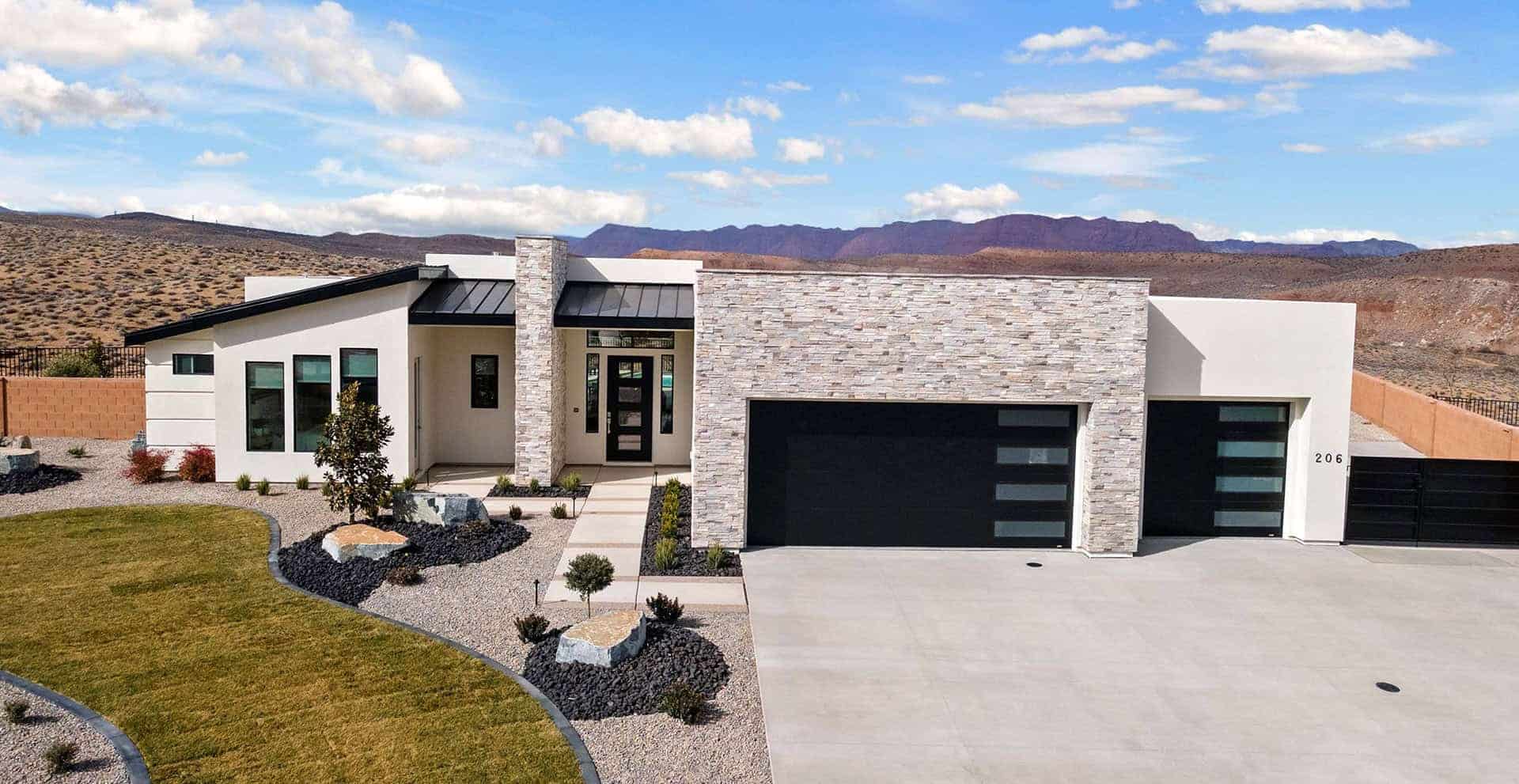 Modern home with two matte black steel and glass garage doors, white stucco and ledger stone exterior, and red rock desert mountains in the background, typical of contemporary construction in St. George, Utah