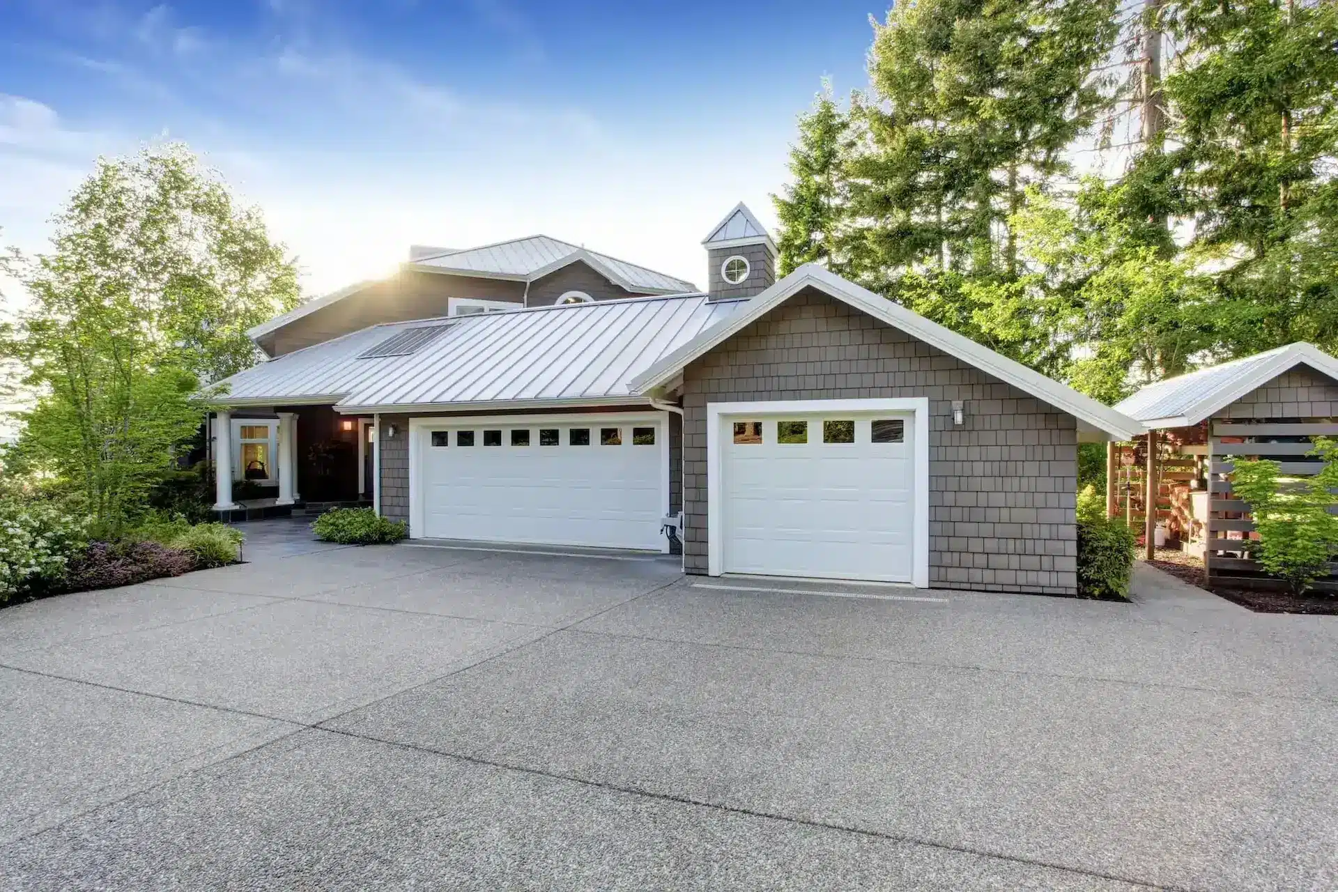 White raised-panel garage doors with window inserts on a craftsman-style home with cedar shake siding and a standing-seam metal roof, showing a two-car and single-car residential garage door installation
