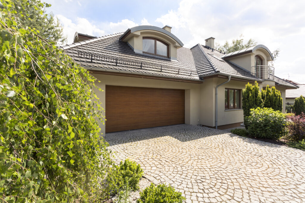Wood-grain finish single garage door on a beige stucco home with a cobblestone driveway and slate tile roof, showing a residential garage door installation with a natural wood appearance