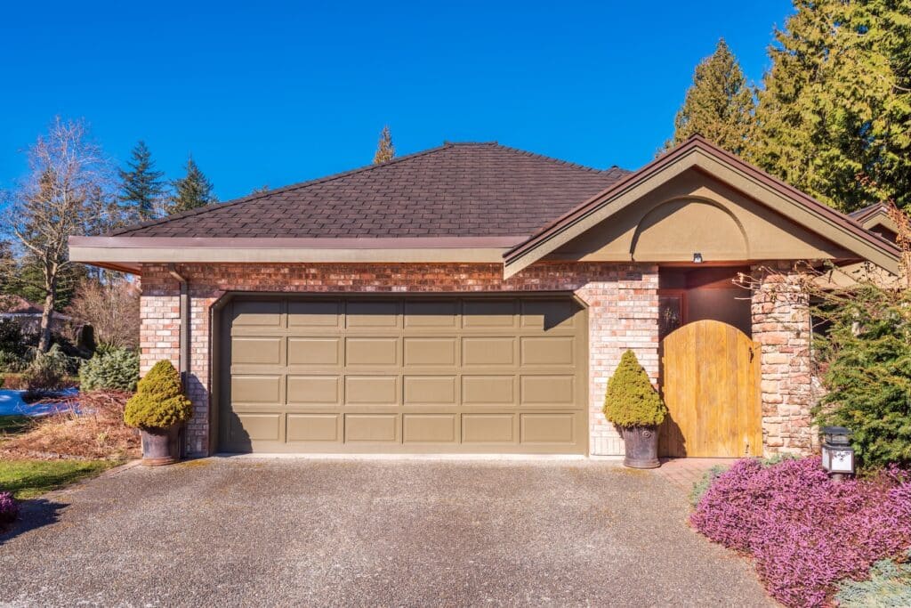 Tan steel raised-panel garage door on a brick home with wood entry door. Residential garage door installation in Utah by Price's Guaranteed Doors