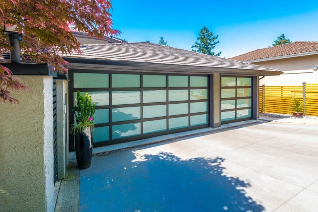 Modern full-view aluminum and frosted glass garage doors with black frames on a contemporary stucco home