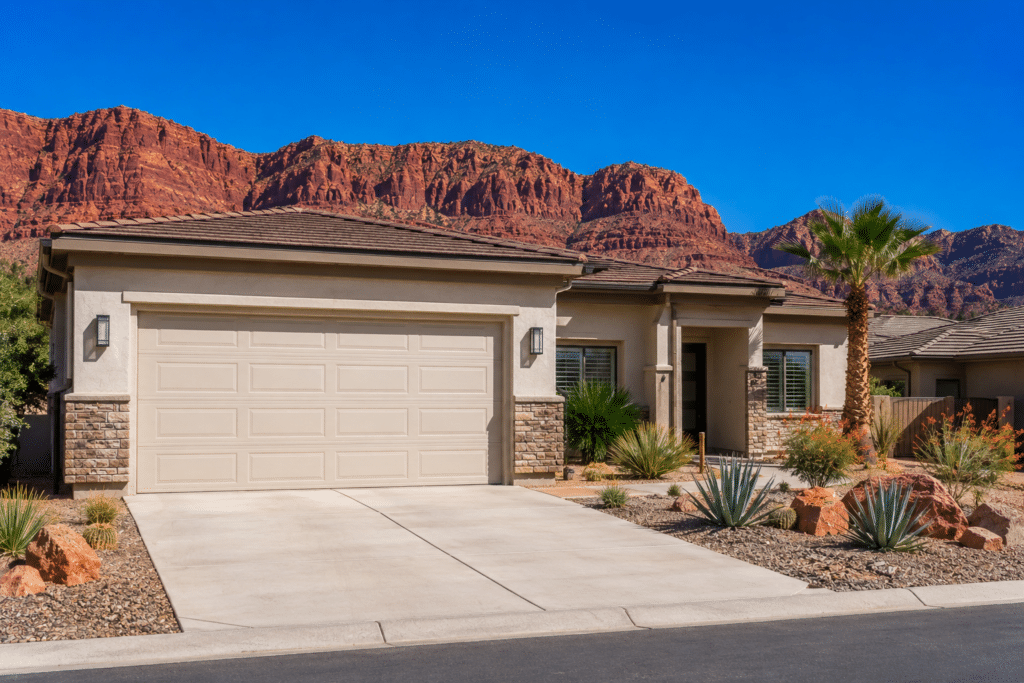 Light beige garage door on a stucco home in St. George, Utah, with red rock cliffs and desert landscaping in the background